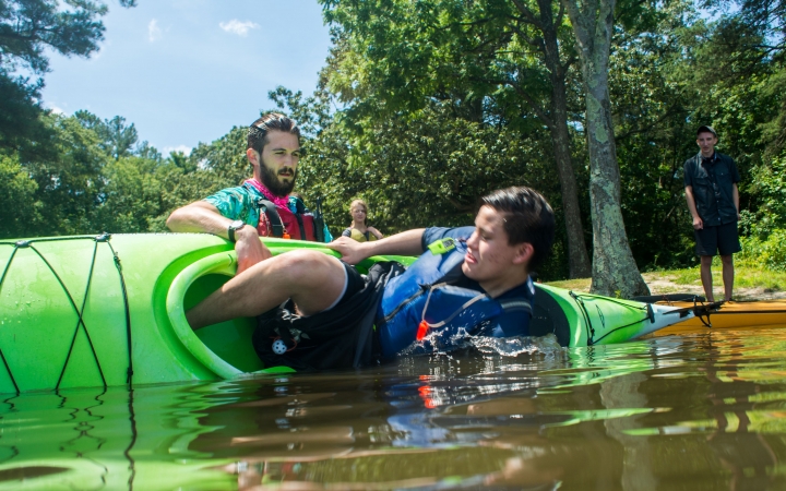 During a safety exercise, a person flips their kayak over while an instructor braces it. 